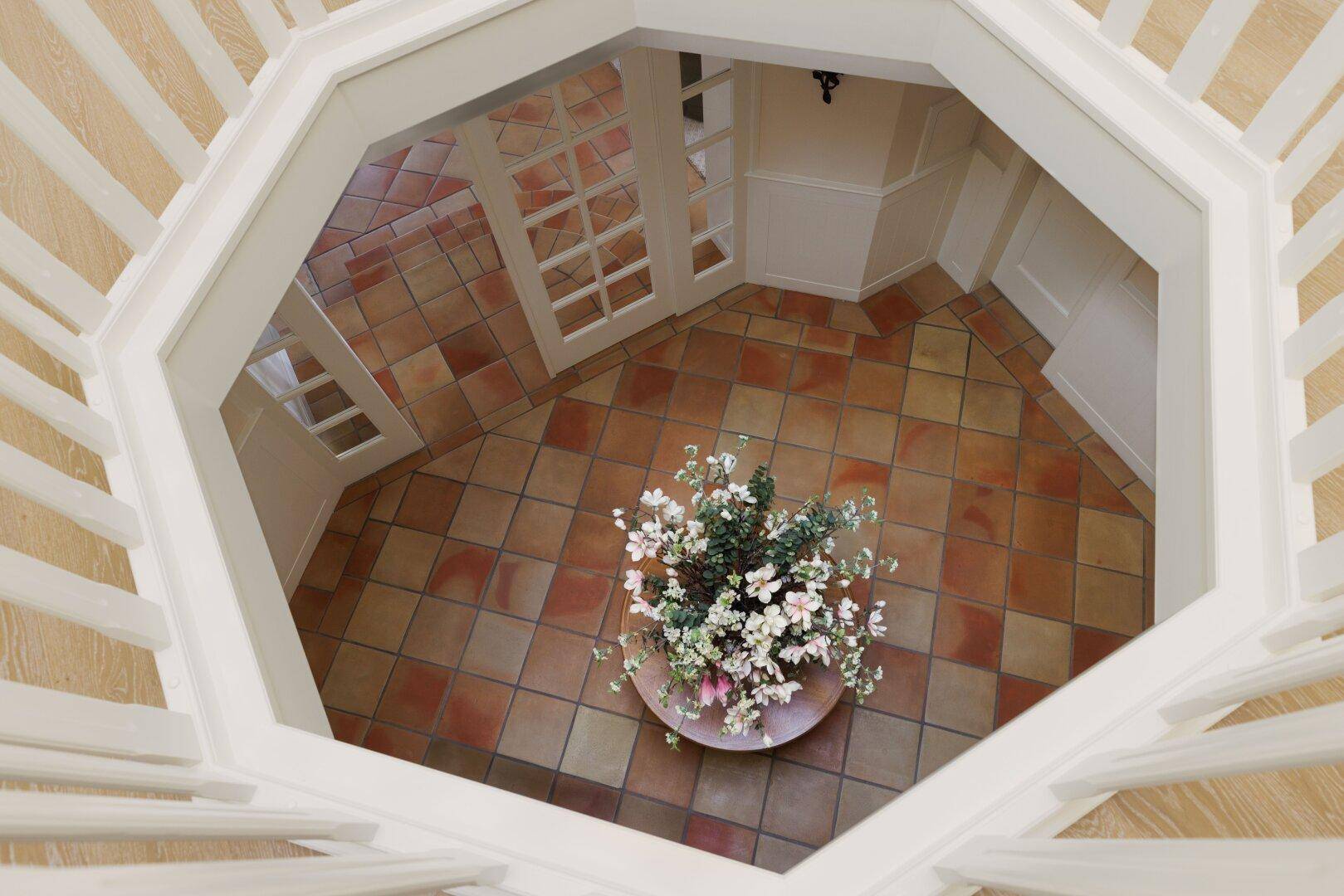 Blick von oben in den hellen Eingangsbereich mit Terrakottaboden und Blumenarrangement.