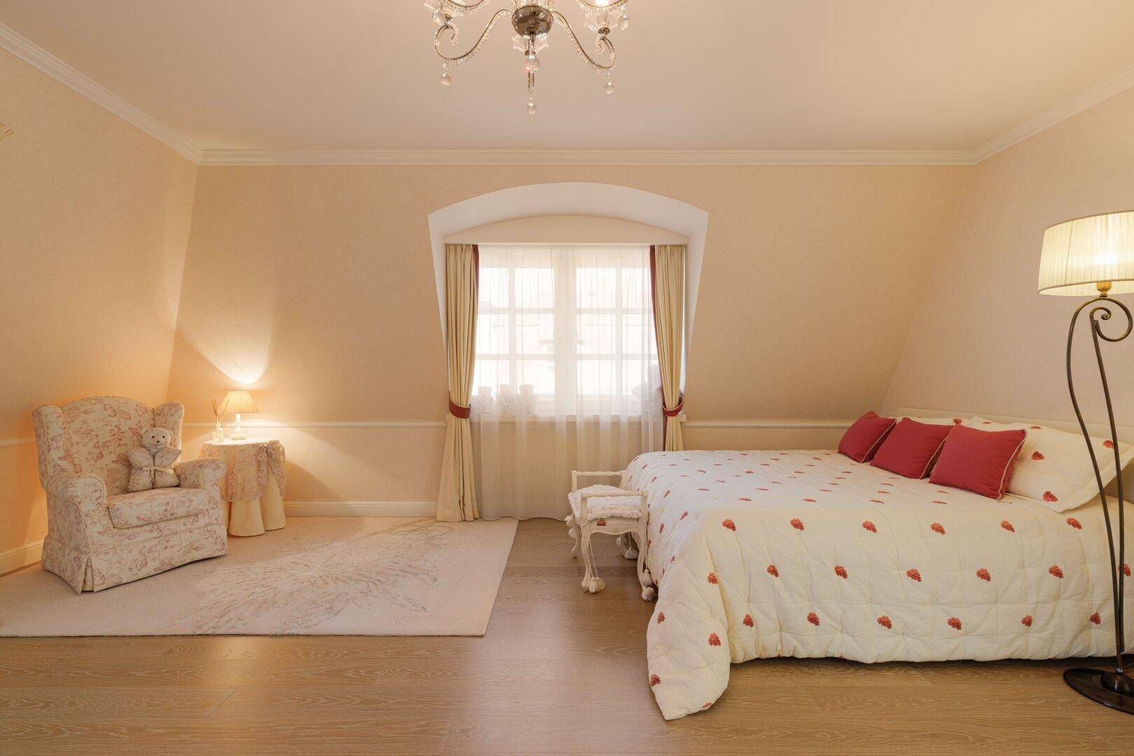 Gemütliches Schlafzimmer mit Holzboden, Sessel und Fenster mit Vorhängen.