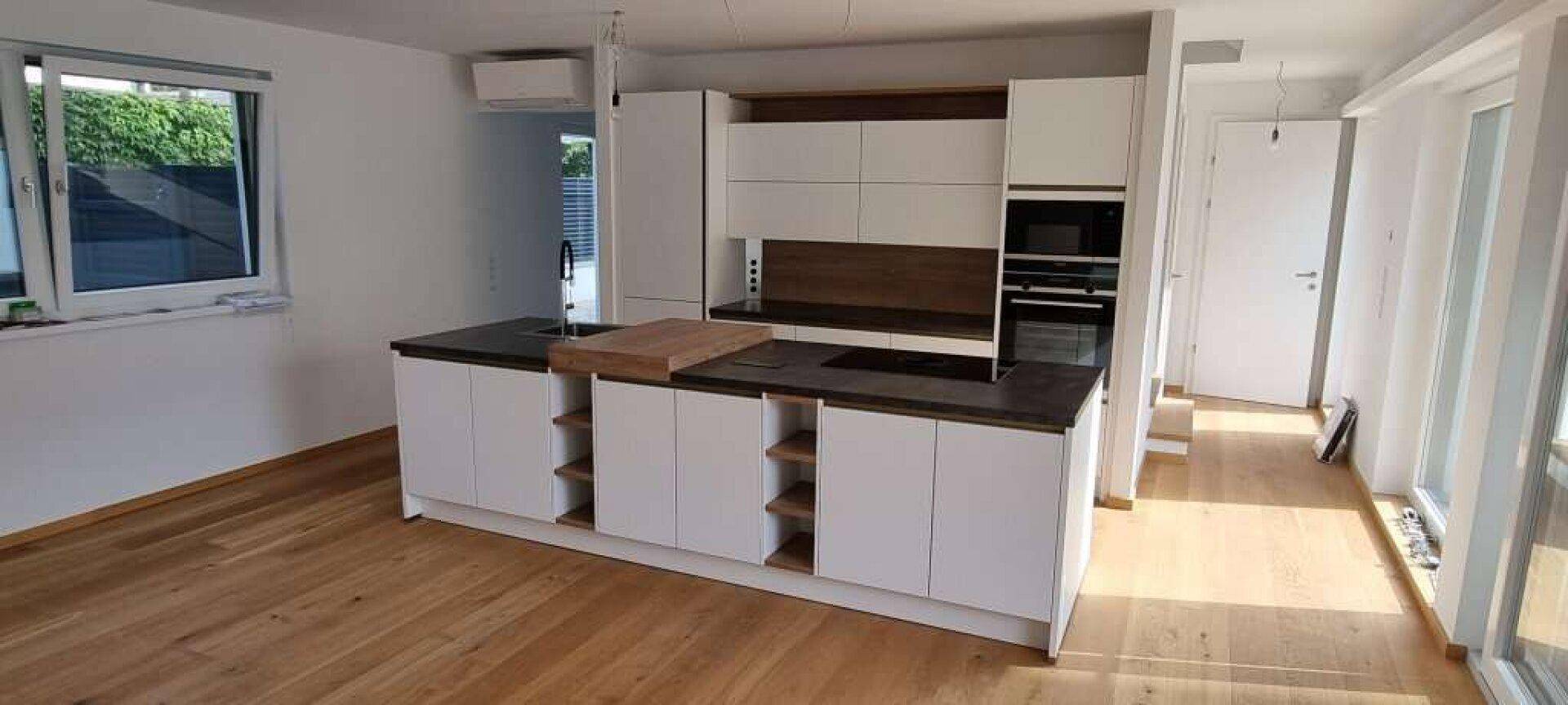 Helle Küche mit Kücheninsel, modernen Geräten und Holzboden, die viel Tageslicht erhält.