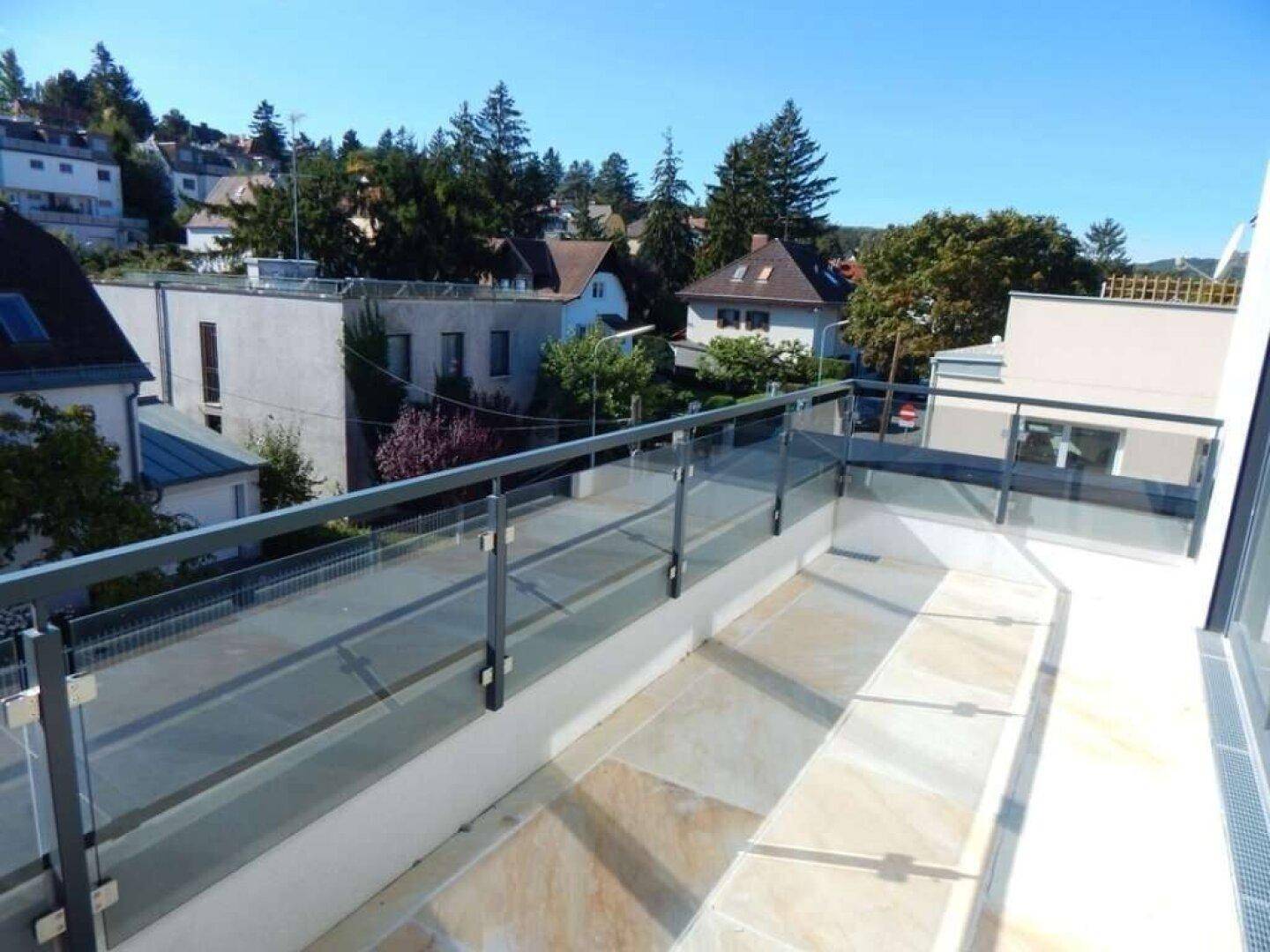 Geräumiger Balkon mit Glasgeländer und weitem Blick über die umliegende Wohngegend und Bäume.