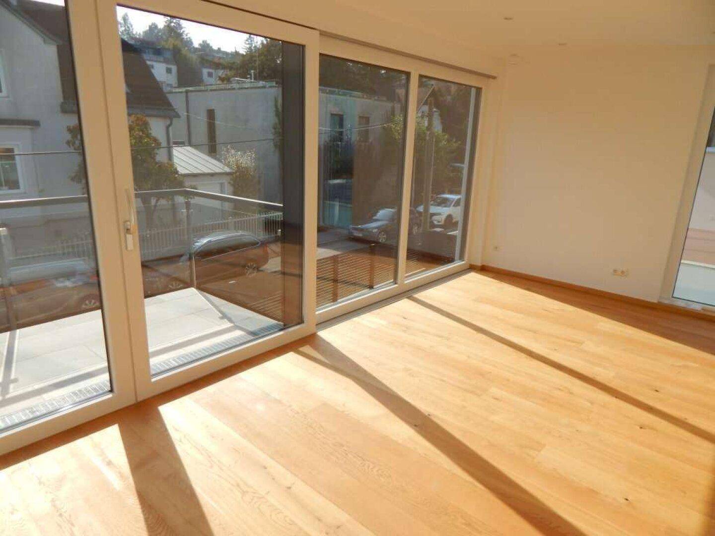 Sonniger Raum mit großen Glasfronten und Holzboden, der einen weiten Blick nach draußen ermöglicht.