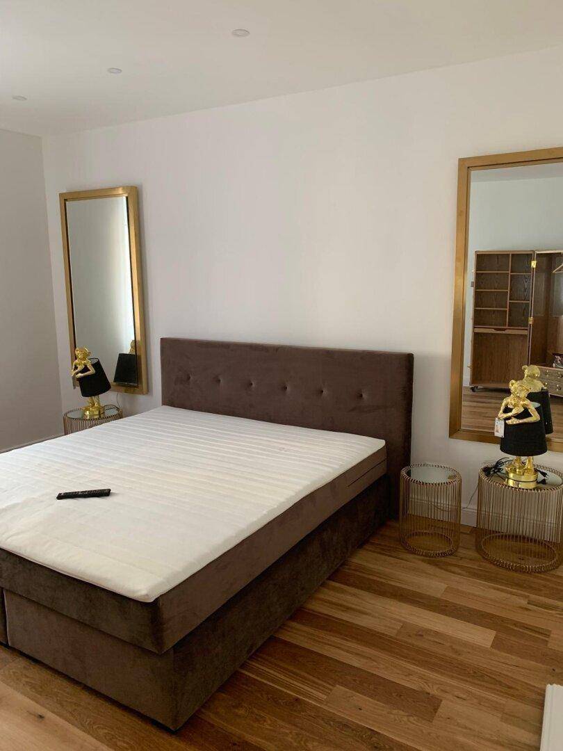 Helles Schlafzimmer mit Doppelbett, Holzboden und großen Wandspiegeln.