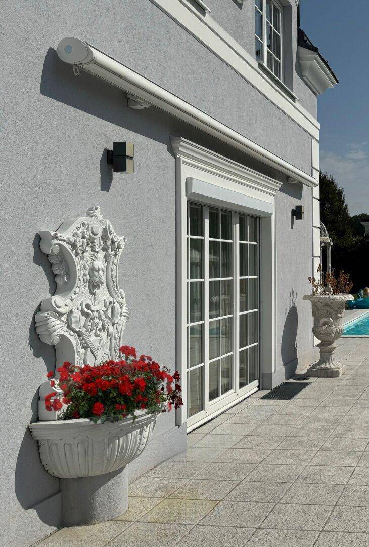 Dekorative Wandverzierung mit Blumenkübel und Rollladen an der Hausfassade.