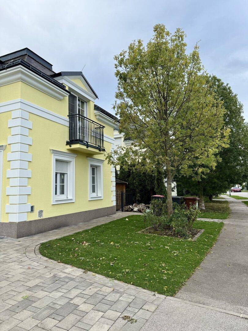 Seitenansicht eines gelben Hauses mit kleinem Vorgarten und Baum.