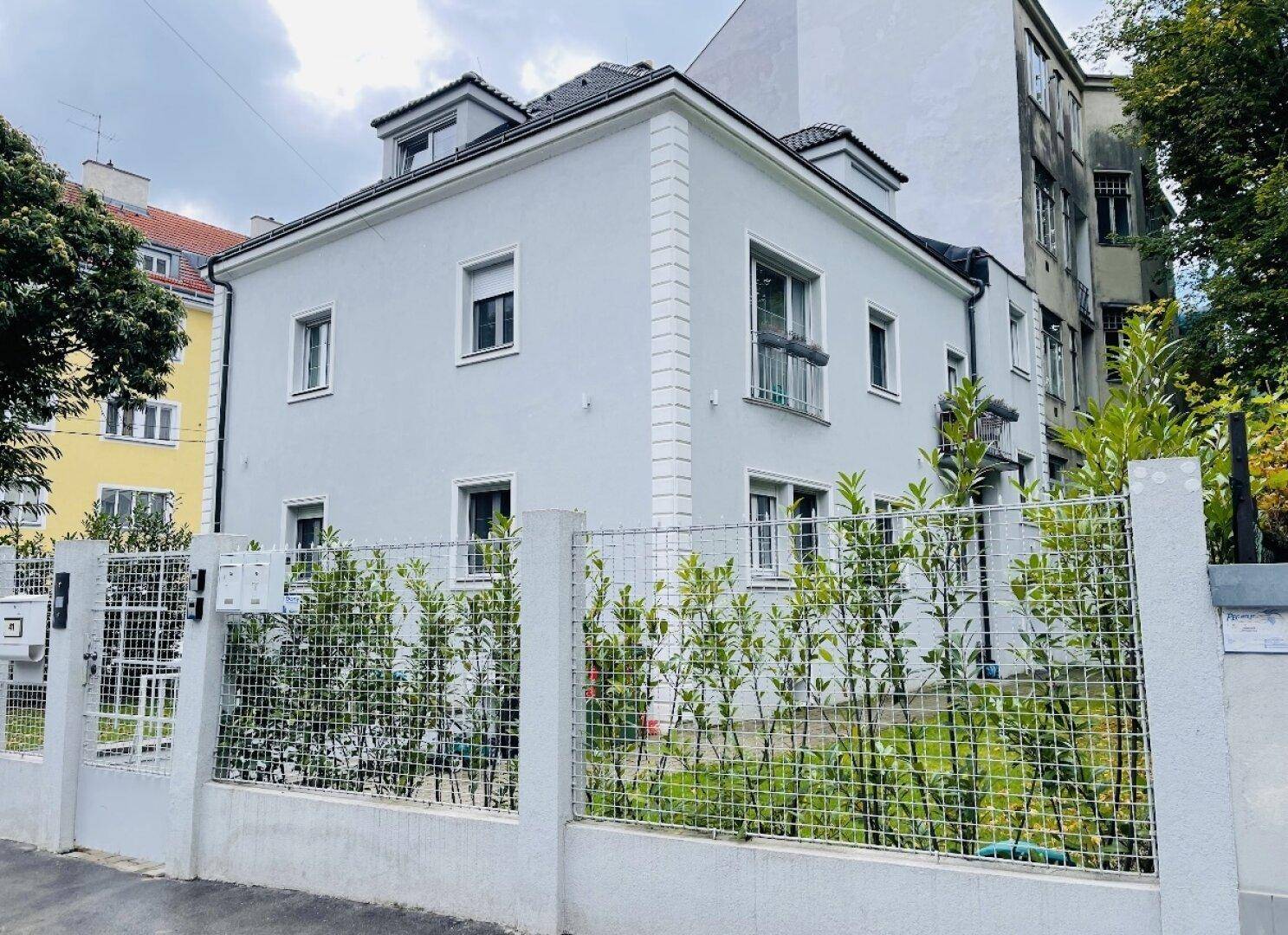 Außenansicht der Villa mit Zaun und umliegender Bepflanzung.
