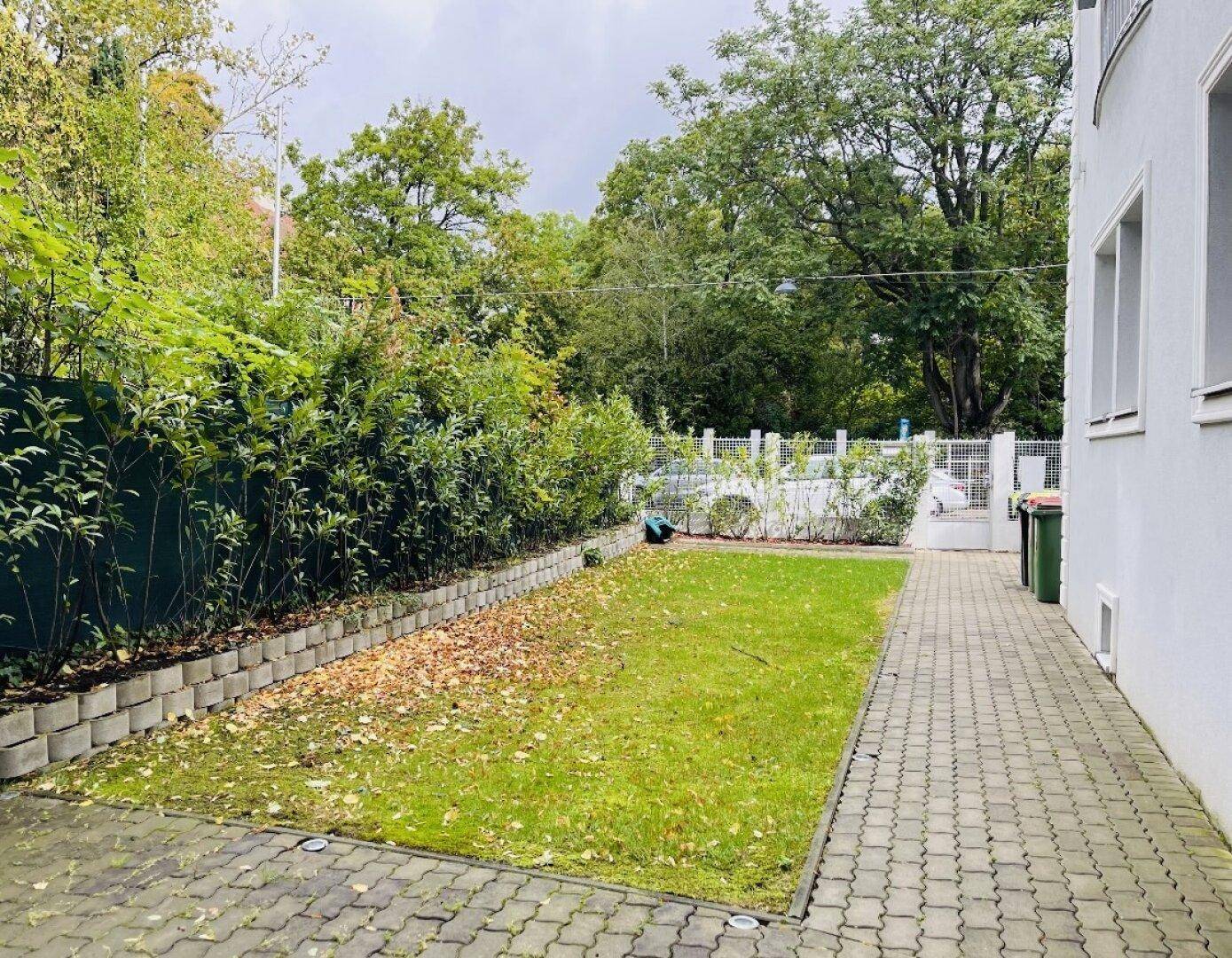 Gepflasterter Weg im Gartenbereich mit Rasenfläche und Hecke.