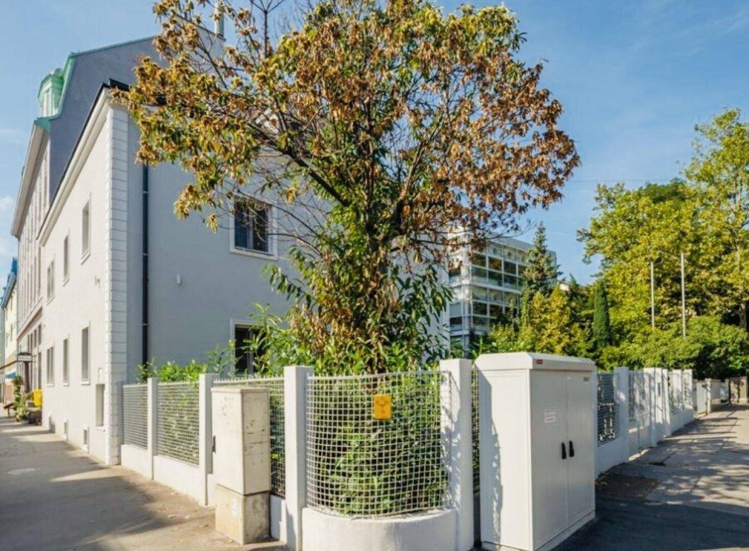 Außenansicht der Villa mit Zaun und Bäumen an einer ruhigen Straße.