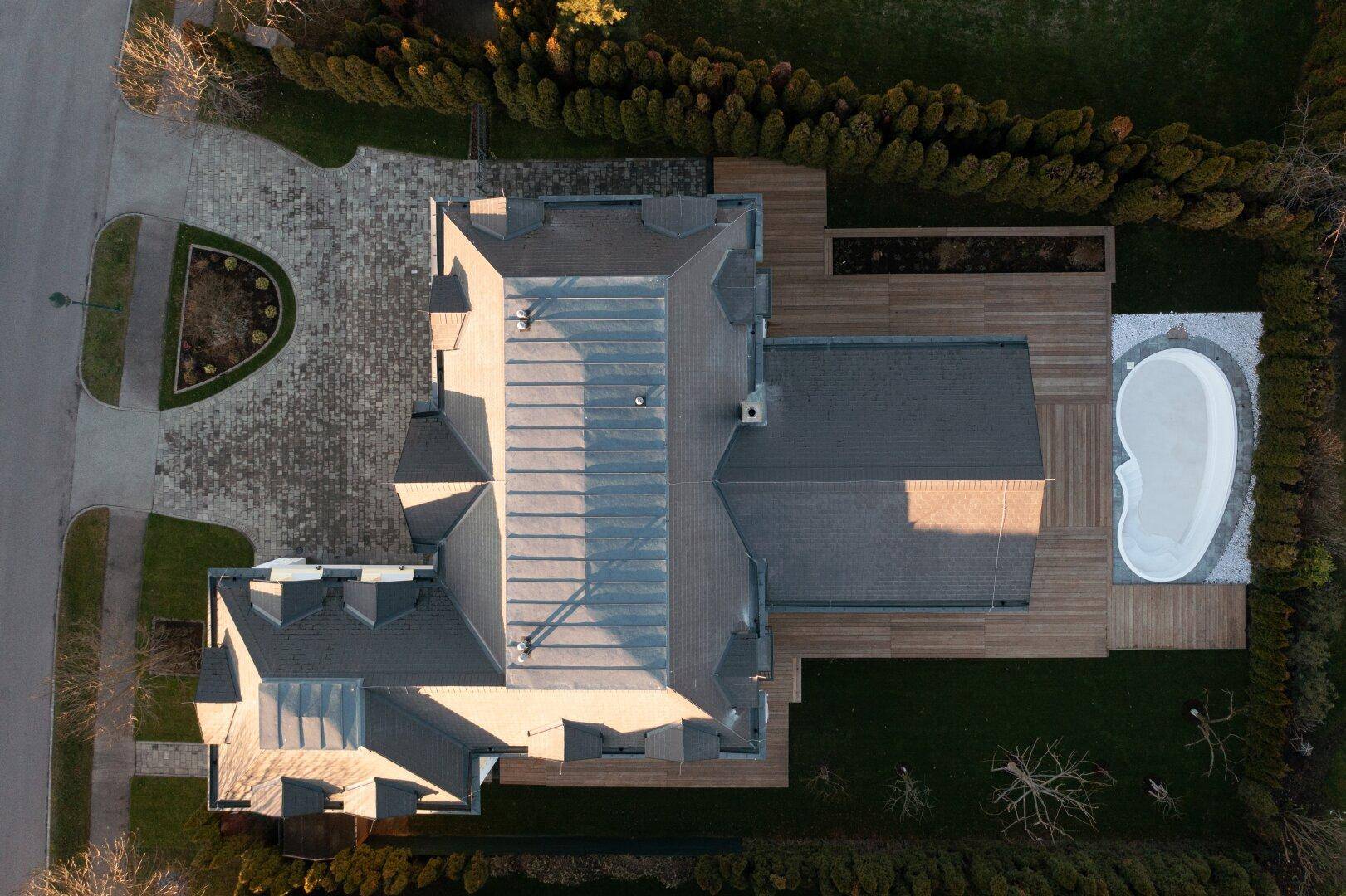 Luftaufnahme eines Hauses mit Pool, Holzdeck und gepflegtem Gartenbereich.