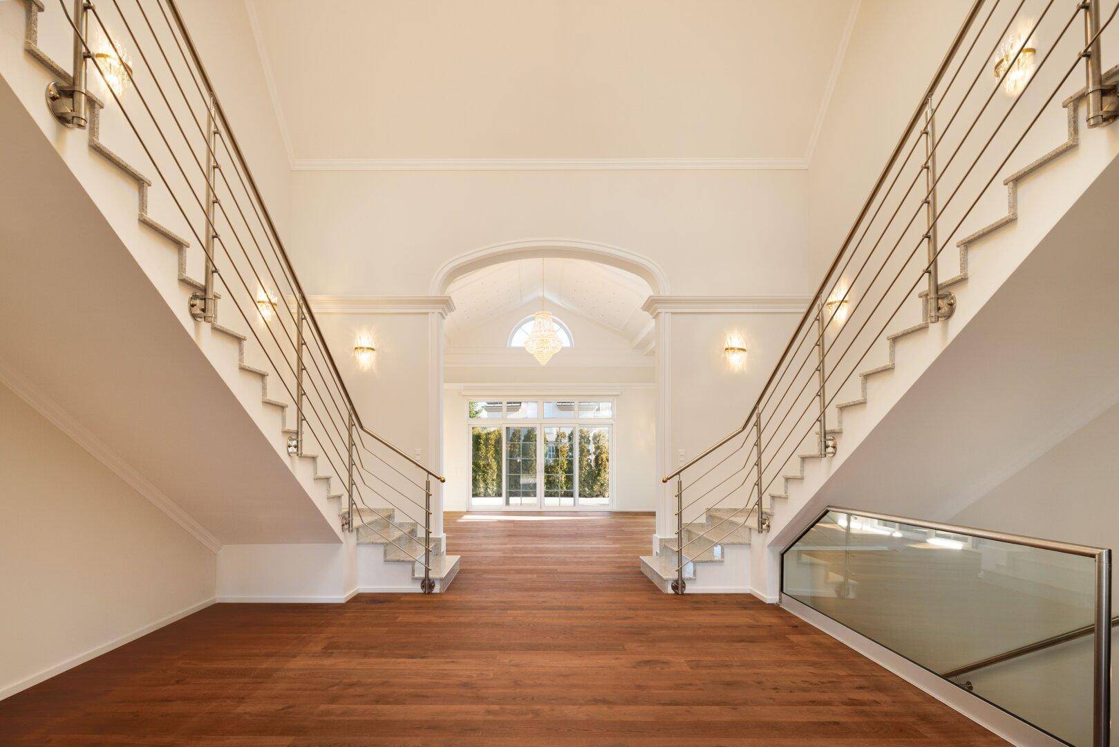 Elegante Eingangshalle mit doppelter Treppe, hohen Decken und Holzboden.
