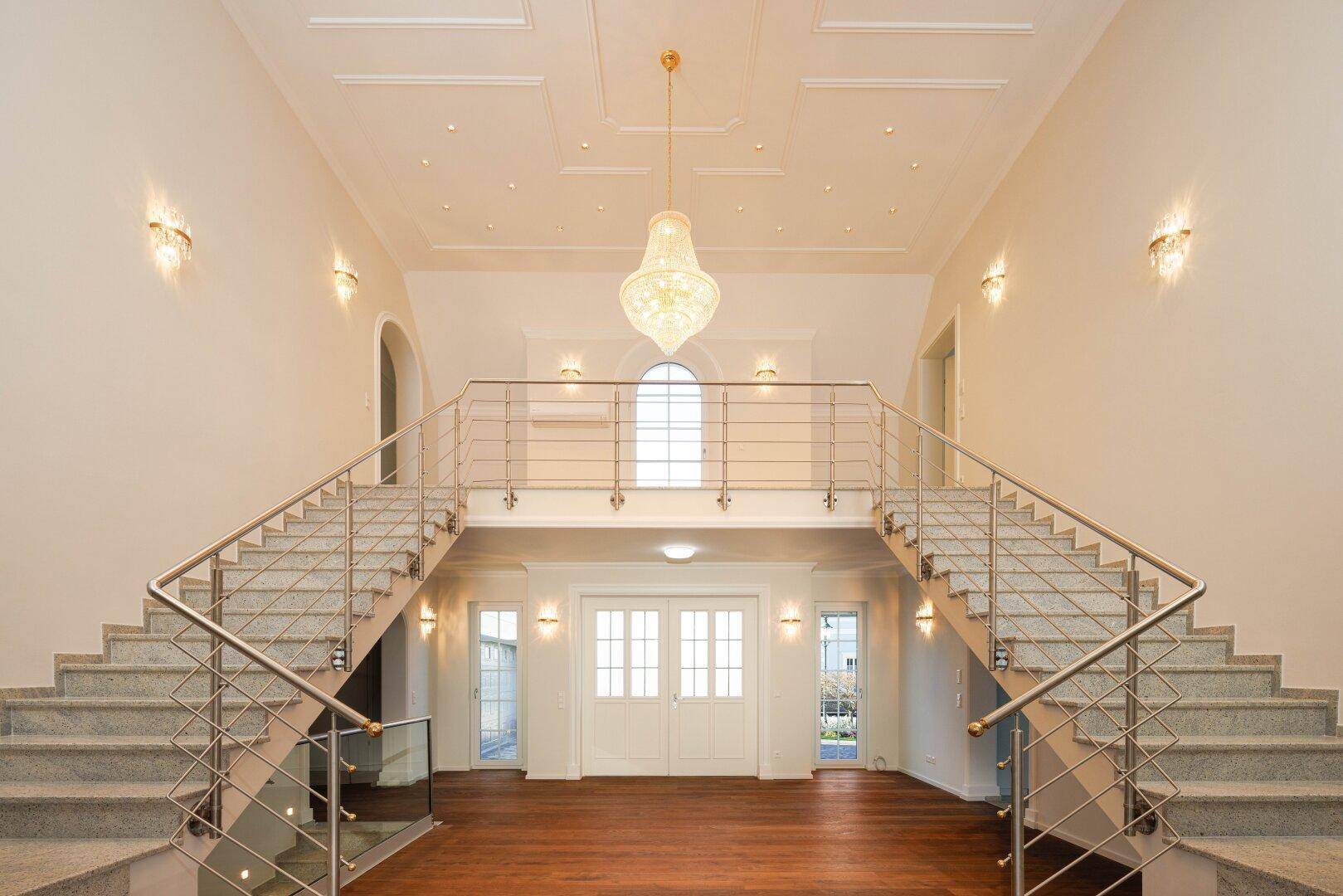 Geräumige Eingangshalle mit Marmortreppe, Kronleuchter und Zugang zu weiteren Räumen.