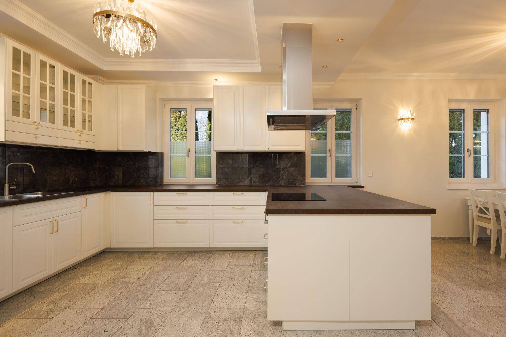 Moderne Küche mit Kochinsel, weißen Schränken und elegantem Kronleuchter.