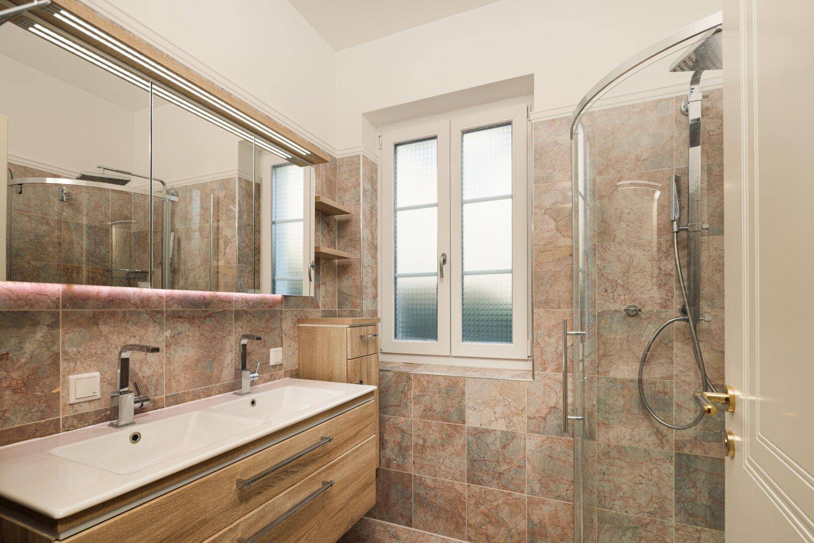 Modernes Badezimmer mit Doppelwaschbecken, Dusche und gemusterten Fliesen.