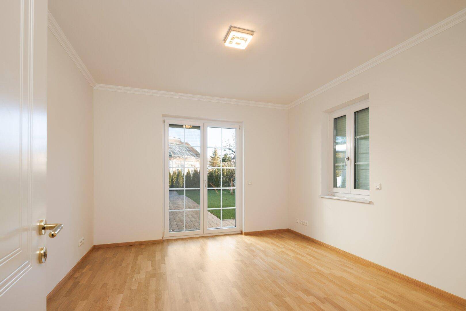Helles Zimmer mit Holzboden und Zugang zum Garten durch große Terrassentüren.