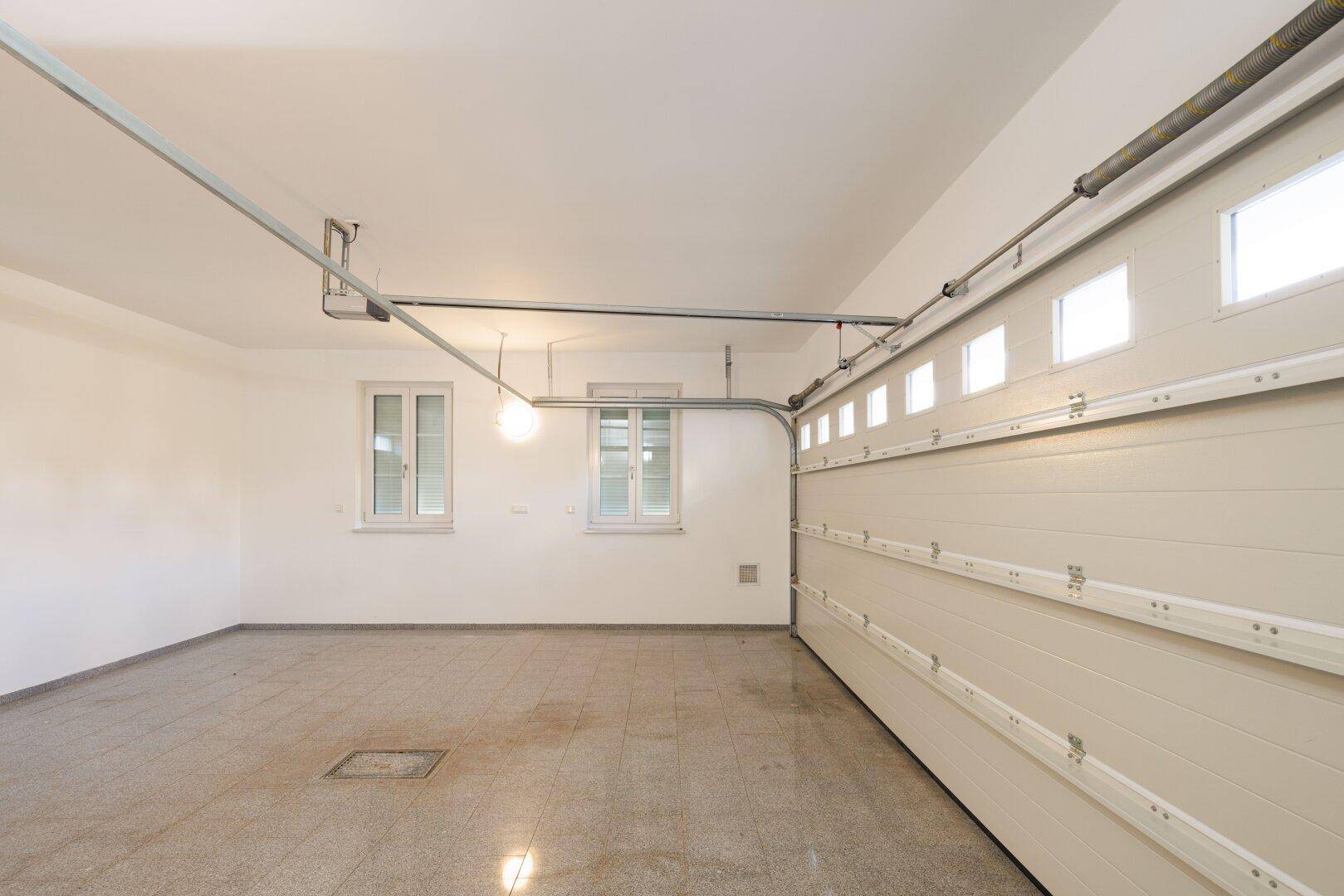 Geräumige Garage mit Fliesenboden und Fenstern für Tageslicht.