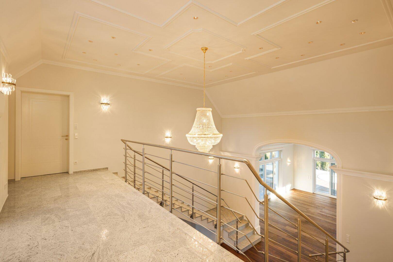 Heller Flur im Obergeschoss mit Marmorboden, Kronleuchter und Blick auf die untere Etage.