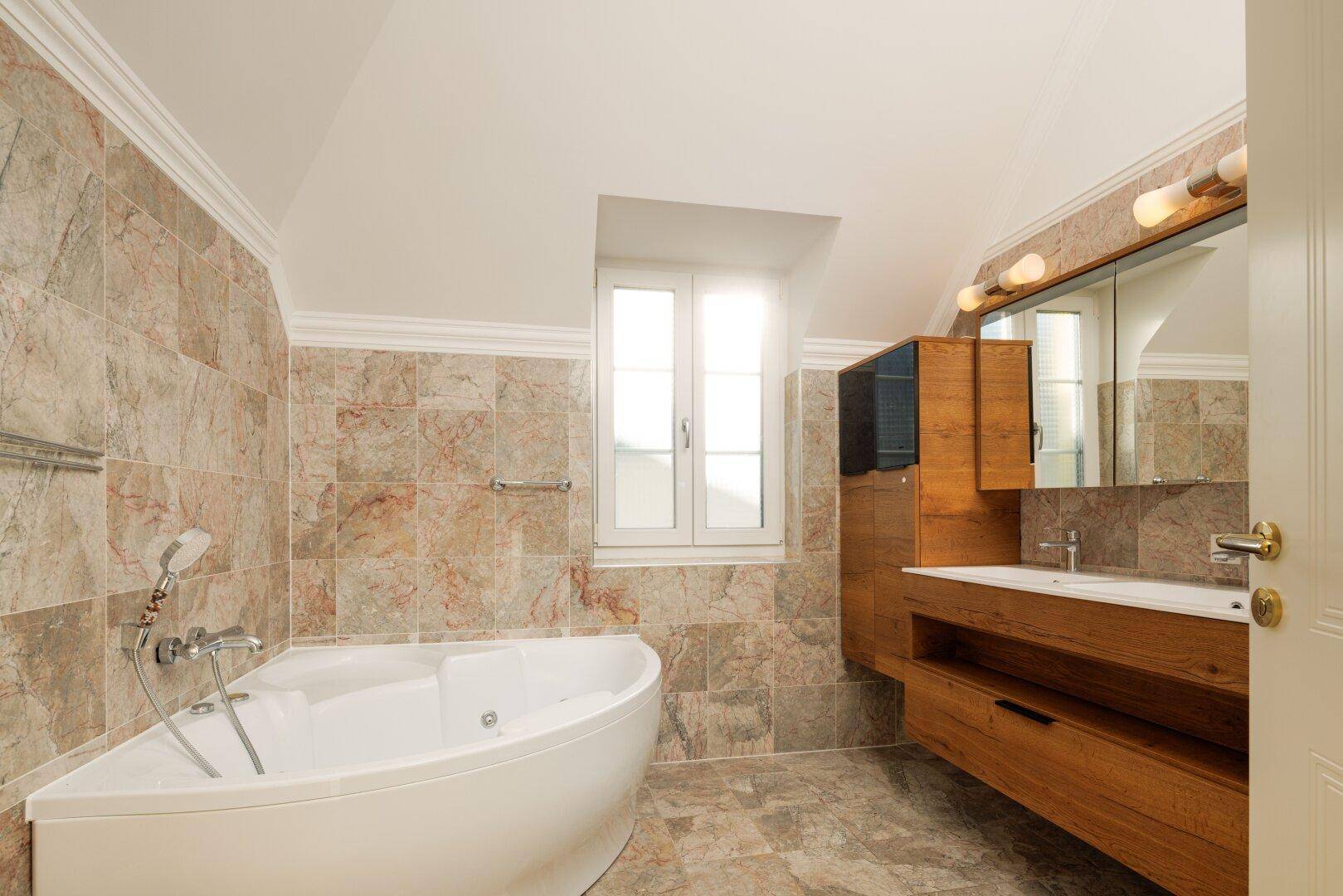 Geräumiges Badezimmer mit Eckbadewanne, Holzwaschtisch und gemusterten Fliesen.