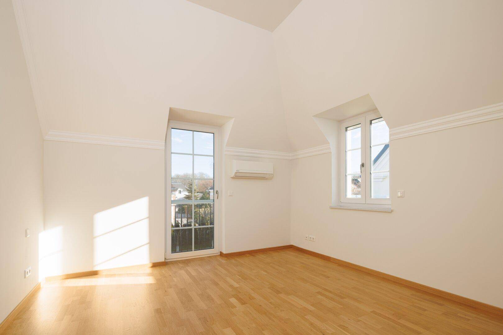 Helles Zimmer mit Holzboden, Dachschräge und französischem Balkon.