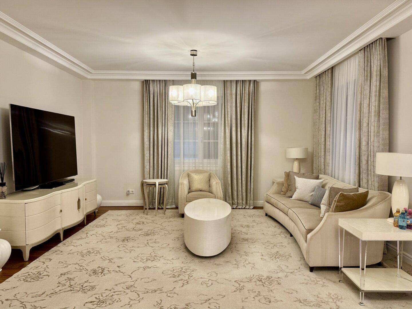Komfortables Wohnzimmer mit großem Sofa, Fernseher und elegantem Teppich auf Holzparkett.