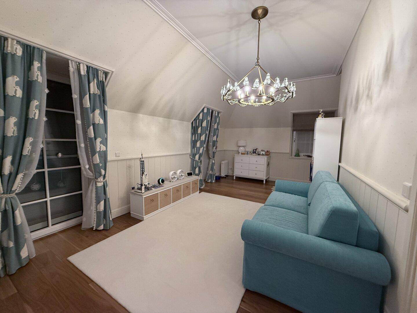 Kinderzimmer mit Dachschräge, blauem Sofa und verspielten Vorhängen.