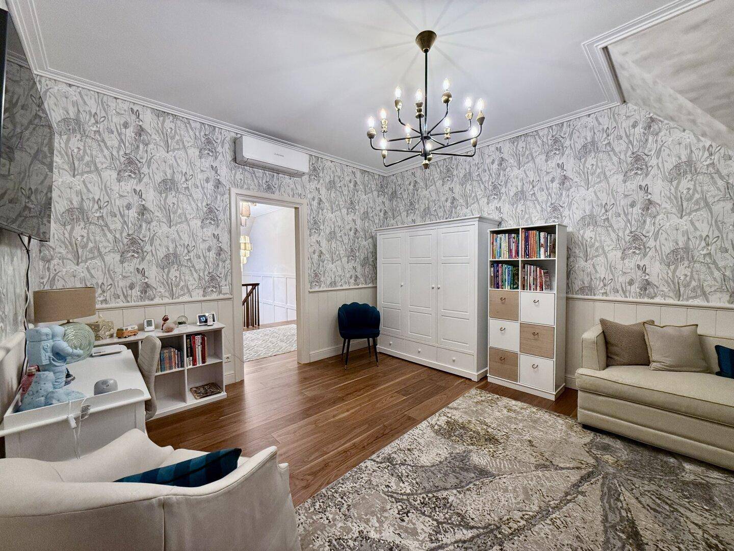 Helles Zimmer mit Schreibtisch, Sofa und gemusterter Tapete.