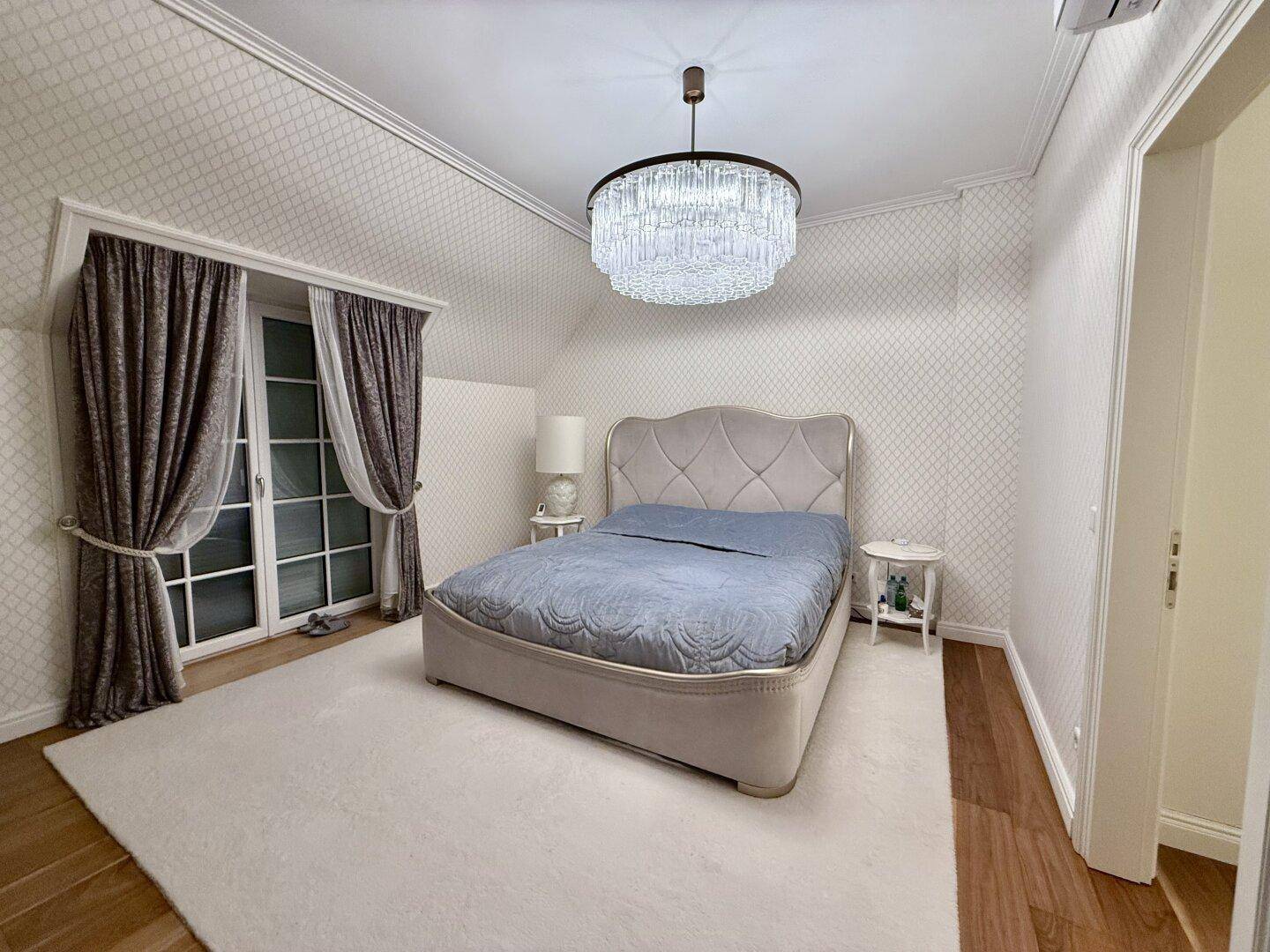 Gemütliches Schlafzimmer mit großem Bett, Teppich und elegantem Kronleuchter.