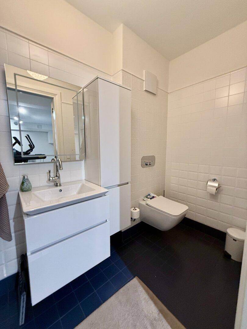 Modernes Gäste-WC mit weißem Waschbecken, Wand-WC und dunklem Fliesenboden.