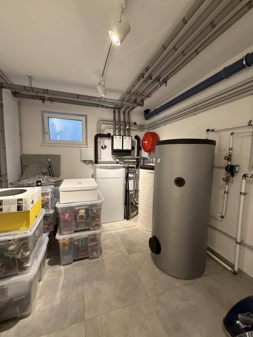 Technikraum im Keller mit Heizungsanlage, Warmwasserspeicher und sichtbaren Rohren.