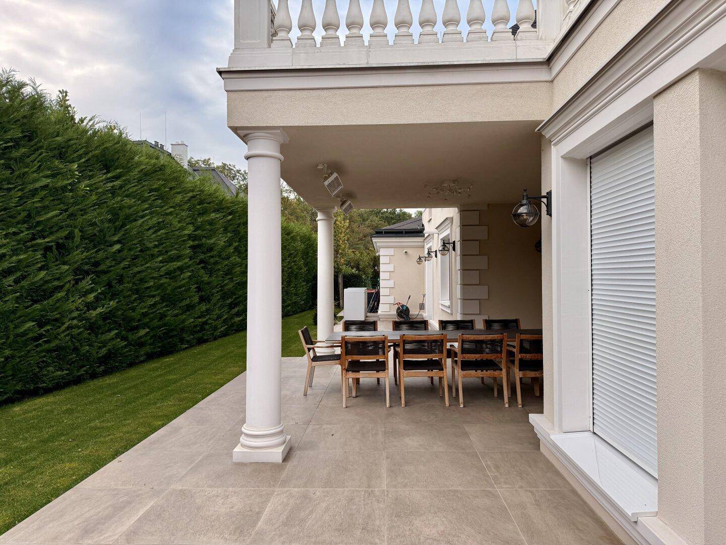 Überdachte Terrasse mit großem Esstisch und Stühlen, ideal für Mahlzeiten im Freien.