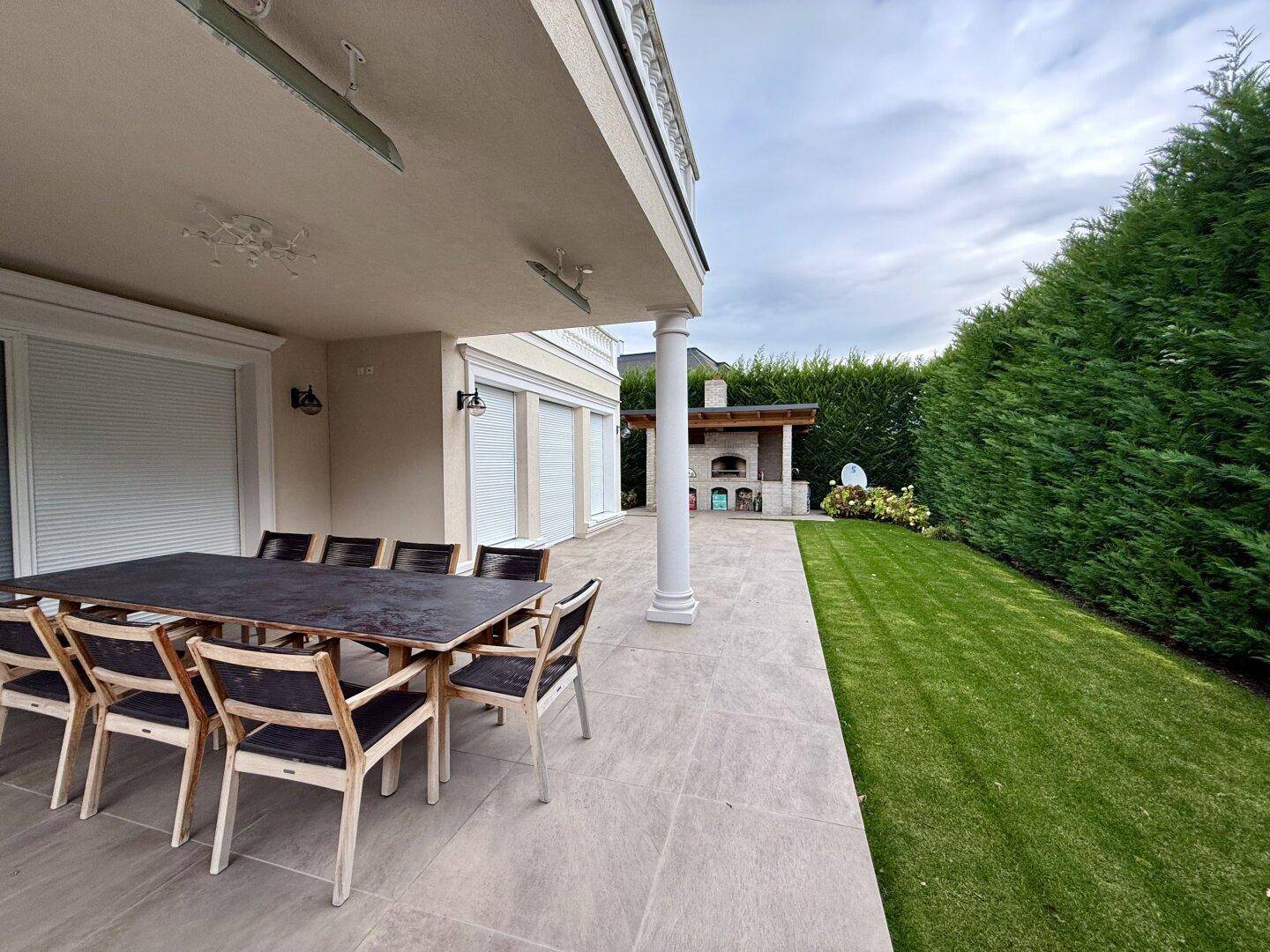 Geräumige Terrasse mit Esstisch und angrenzendem gepflegten Rasenbereich.