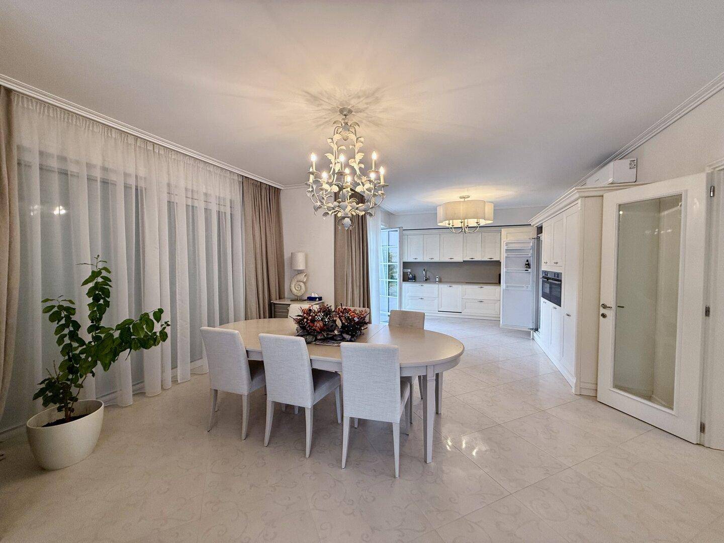 Offener Wohn-Essbereich mit elegantem Esstisch und moderner Einbauküche im Hintergrund.