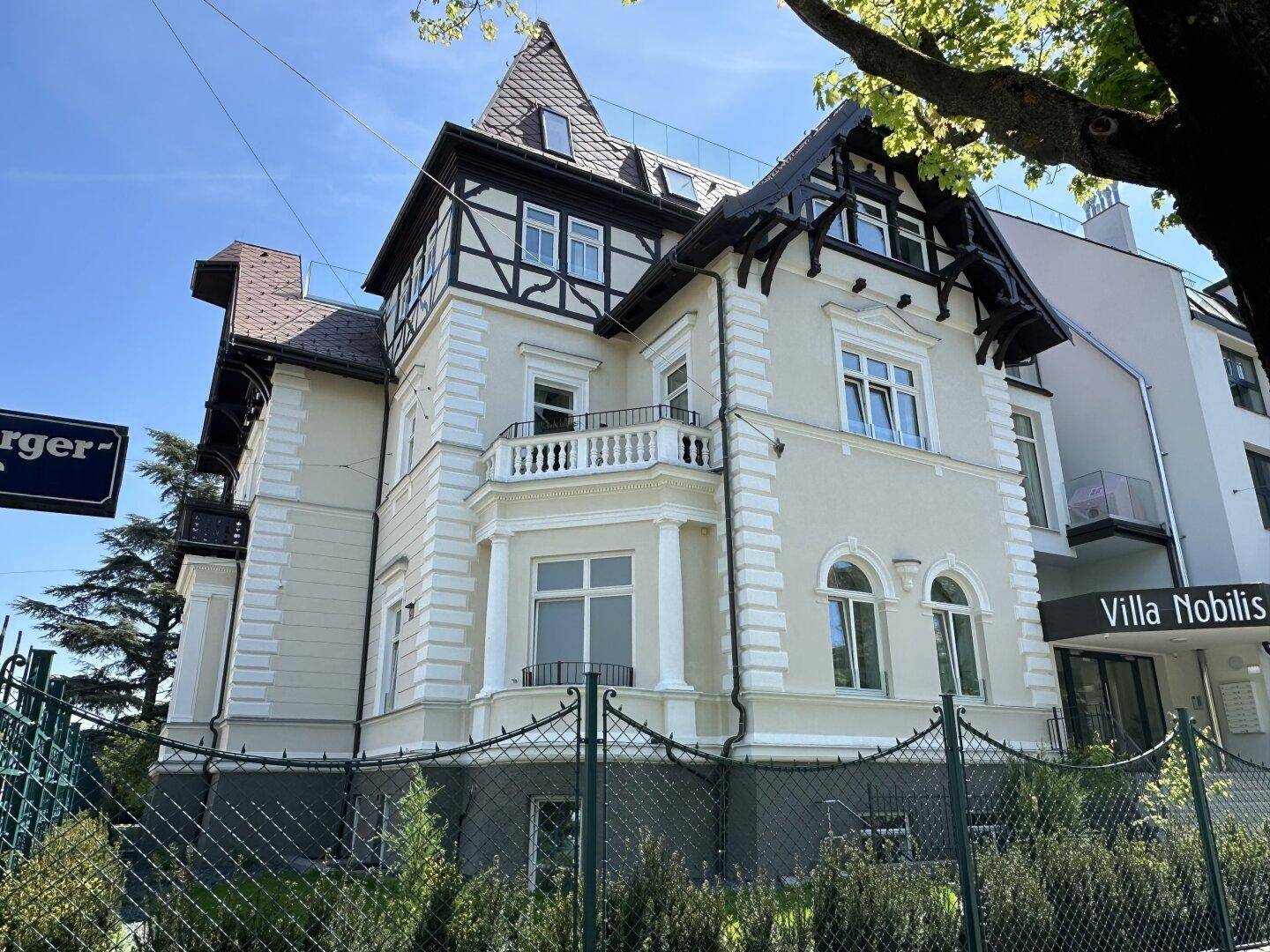 Historische Villa mit aufwendigen Details und einem modernen Anbau unter strahlendem Himmel.
