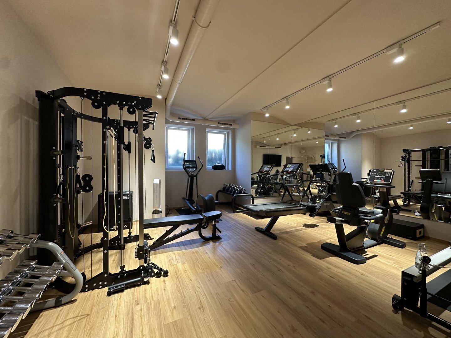 Gut ausgestatteter Fitnessraum mit verschiedenen Trainingsgeräten und großen Spiegeln.