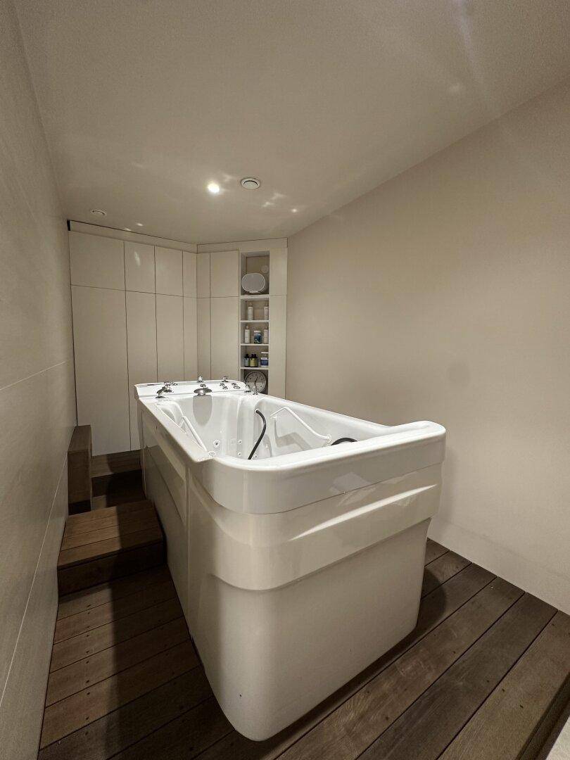 Modernes Badezimmer mit großer Badewanne, Holzfußboden und praktischen Einbauschränken.