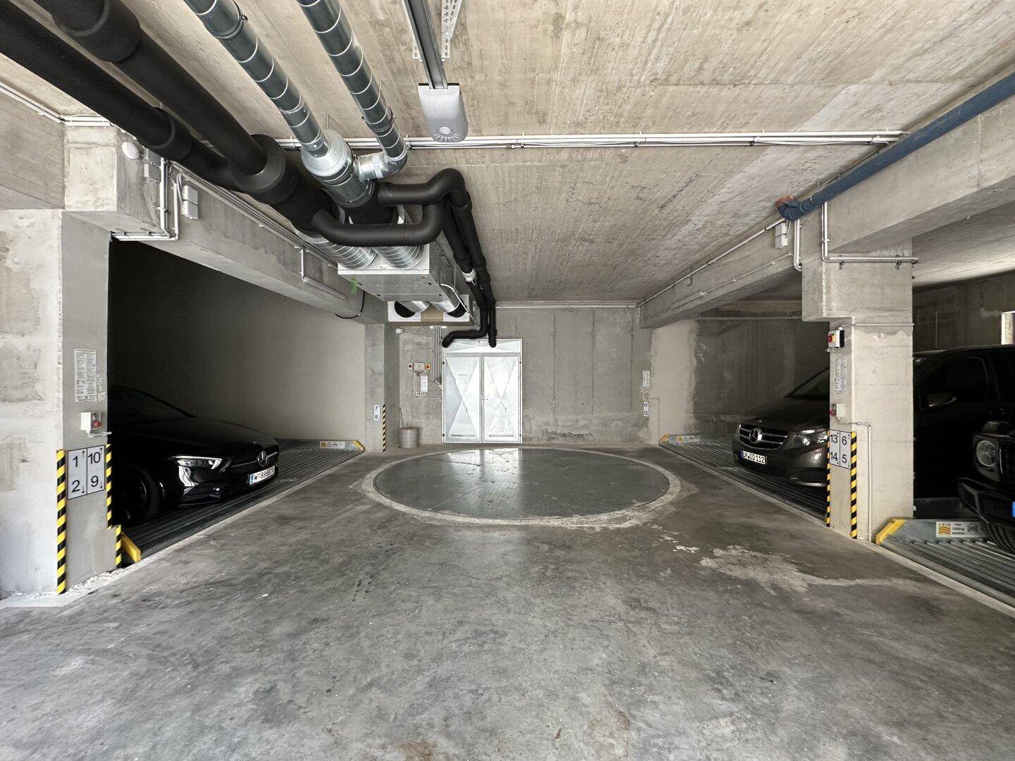 Tiefgarage mit Betonwänden, sichtbaren Leitungen und modernen Parksystemen für Fahrzeuge.