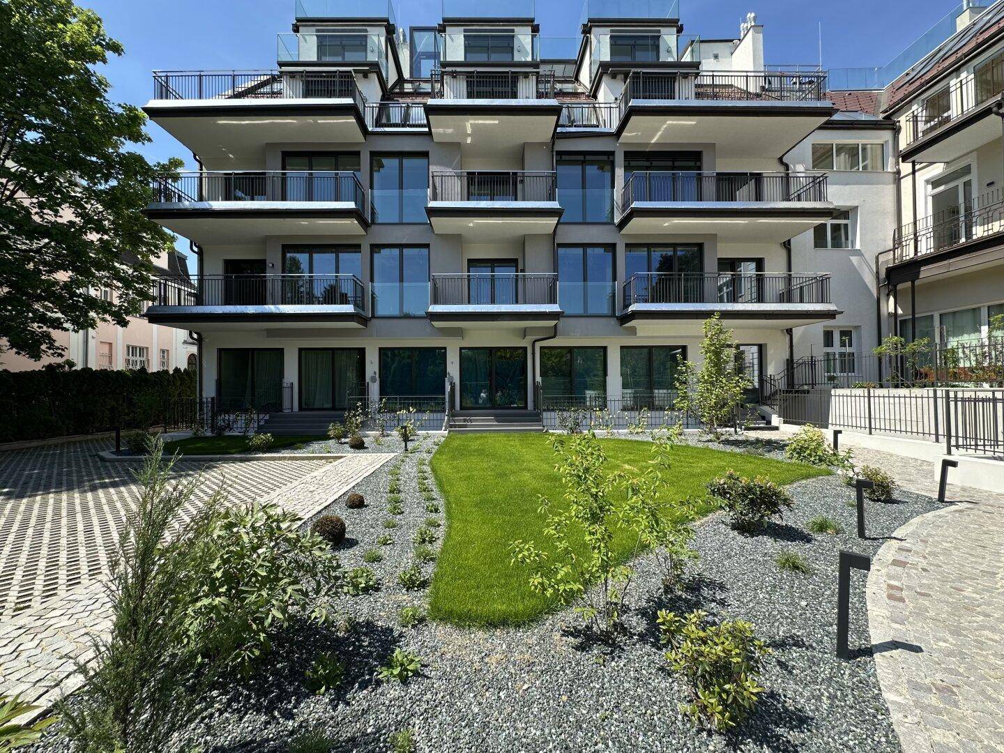 Moderne Wohnanlage mit mehreren Balkonen, gepflegtem Garten und Zufahrt.