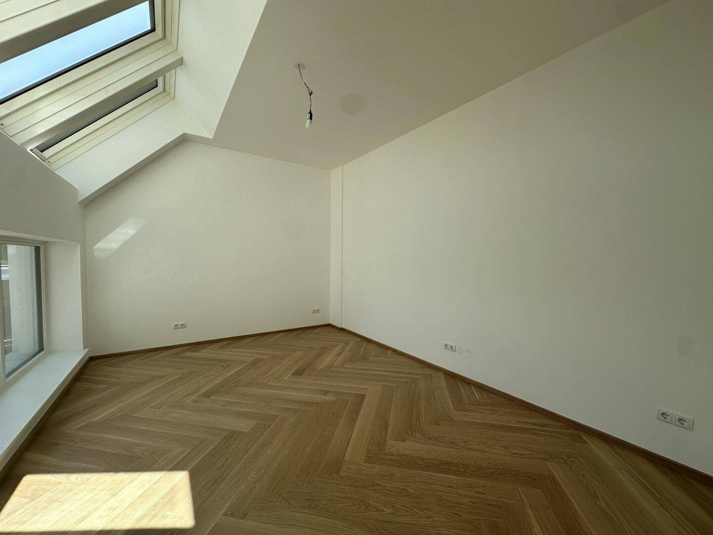 Dachgeschosszimmer mit schrägem Dach, Fischgrätparkett und großem Dachfenster für viel Tageslicht.