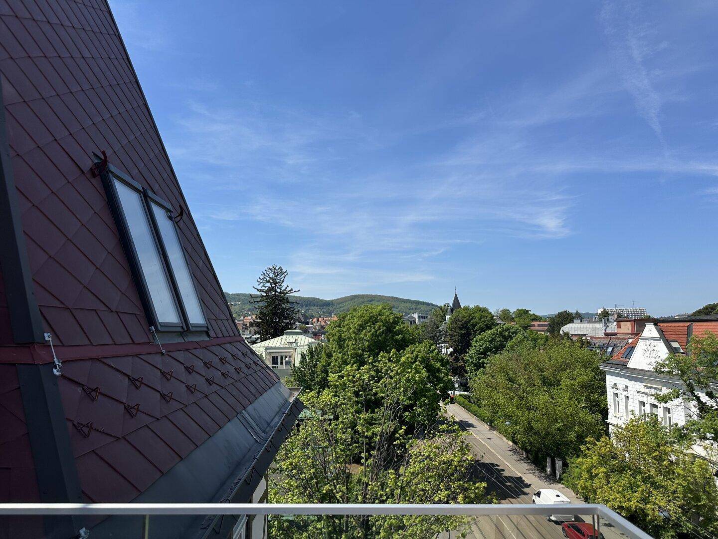 Weitblick über die Stadt mit grünen Bäumen und Bergen im Hintergrund von einem Balkon.