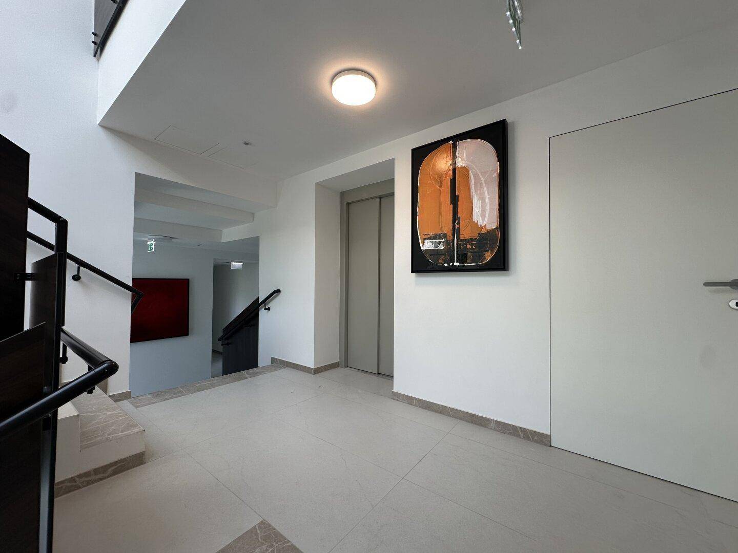 Moderner Treppenaufgang und Aufzugsbereich mit Kunstwerken an den Wänden.