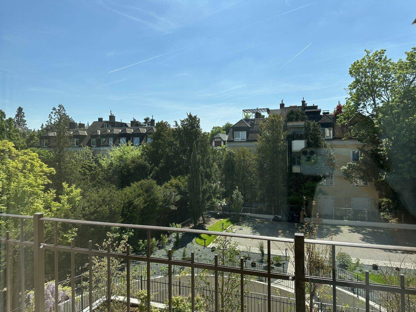 Grüne Aussicht auf Bäume und umliegende Gebäude von einem Balkon oder Fenster aus.
