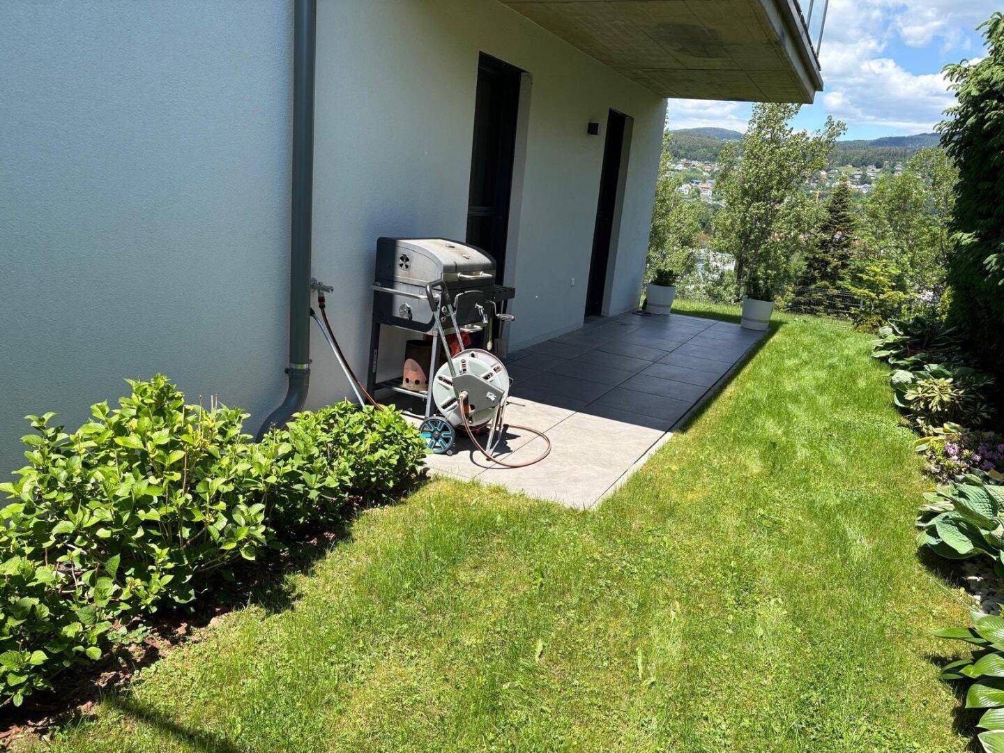 Kleiner Terrassenbereich mit Grill und Zugang zum grünen Garten.