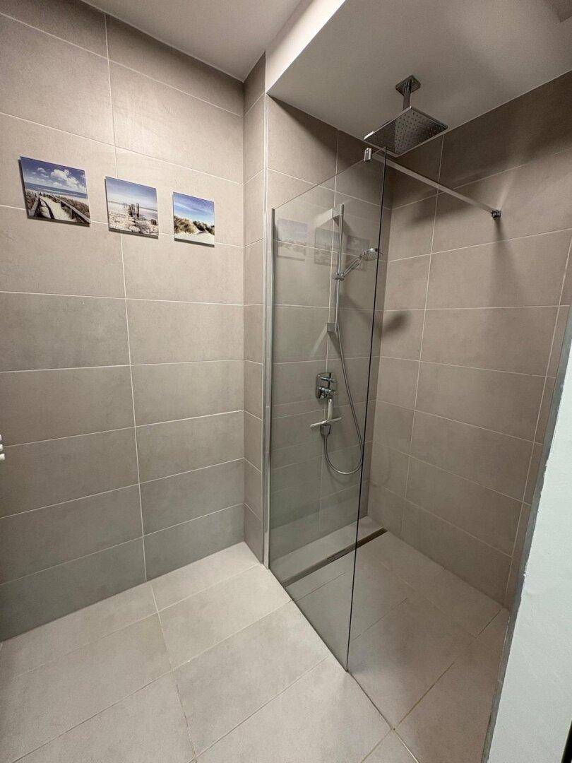 Modernes Badezimmer mit grauen Fliesen, ebenerdiger Dusche und Regenduschkopf.
