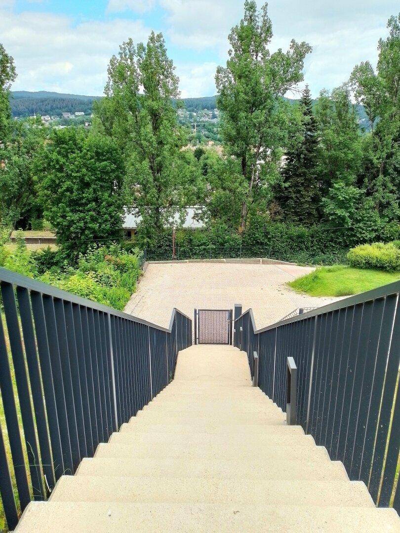 Außentreppe mit dunklem Geländer führt zu einem unteren Bereich mit Bäumen.