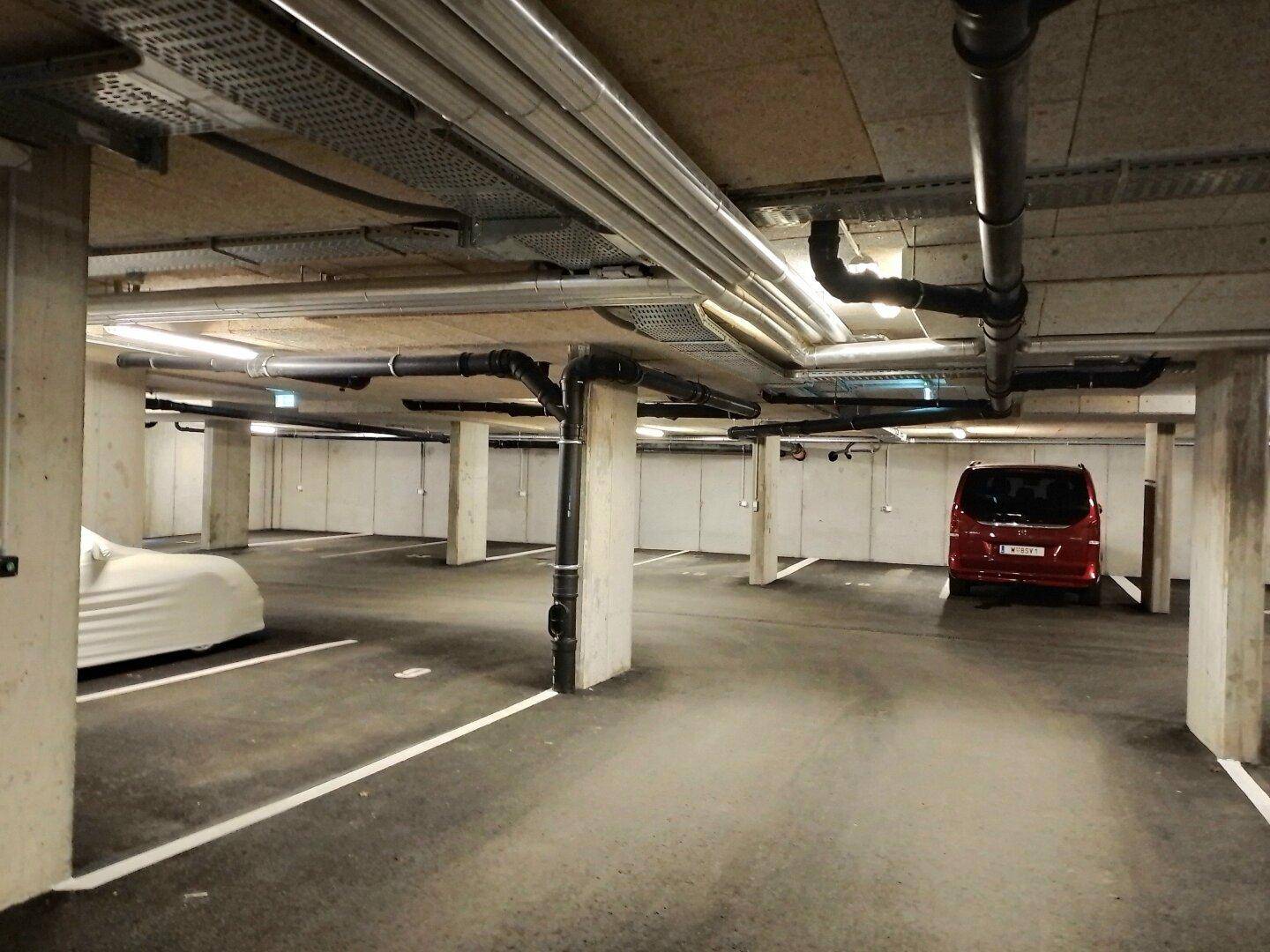 Tiefgarage mit mehreren Stellplätzen und sichtbaren Installationen an der Decke.