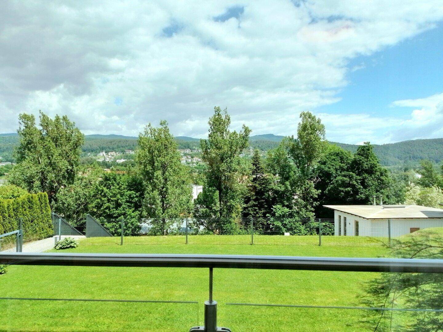 Weitblick über grüne Hügel und Bäume von einem Balkon mit Rasenfläche im Vordergrund.