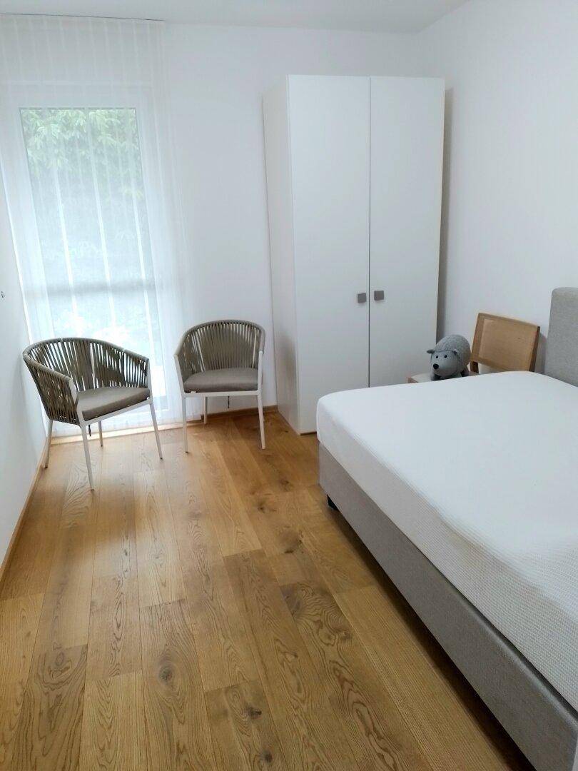 Schlafzimmer mit Holzboden, weißem Kleiderschrank und großem Fenster.