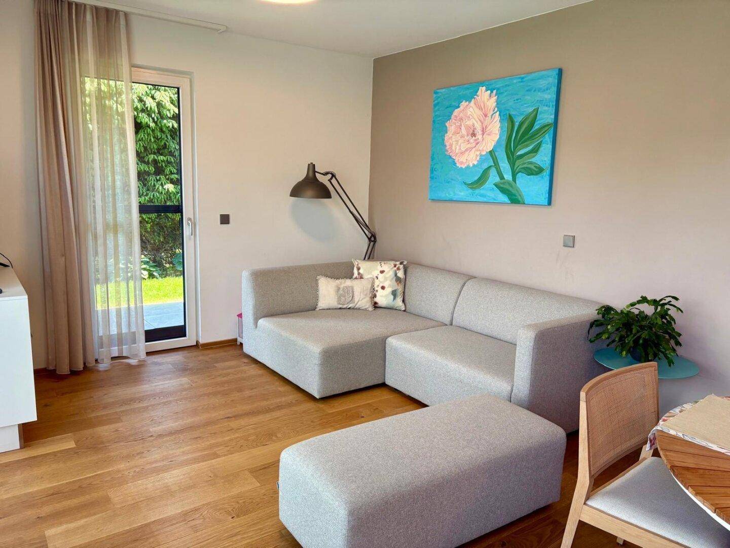 Wohnbereich mit modernem Sofa, Holzboden und Zugang zu einem Garten oder Balkon.