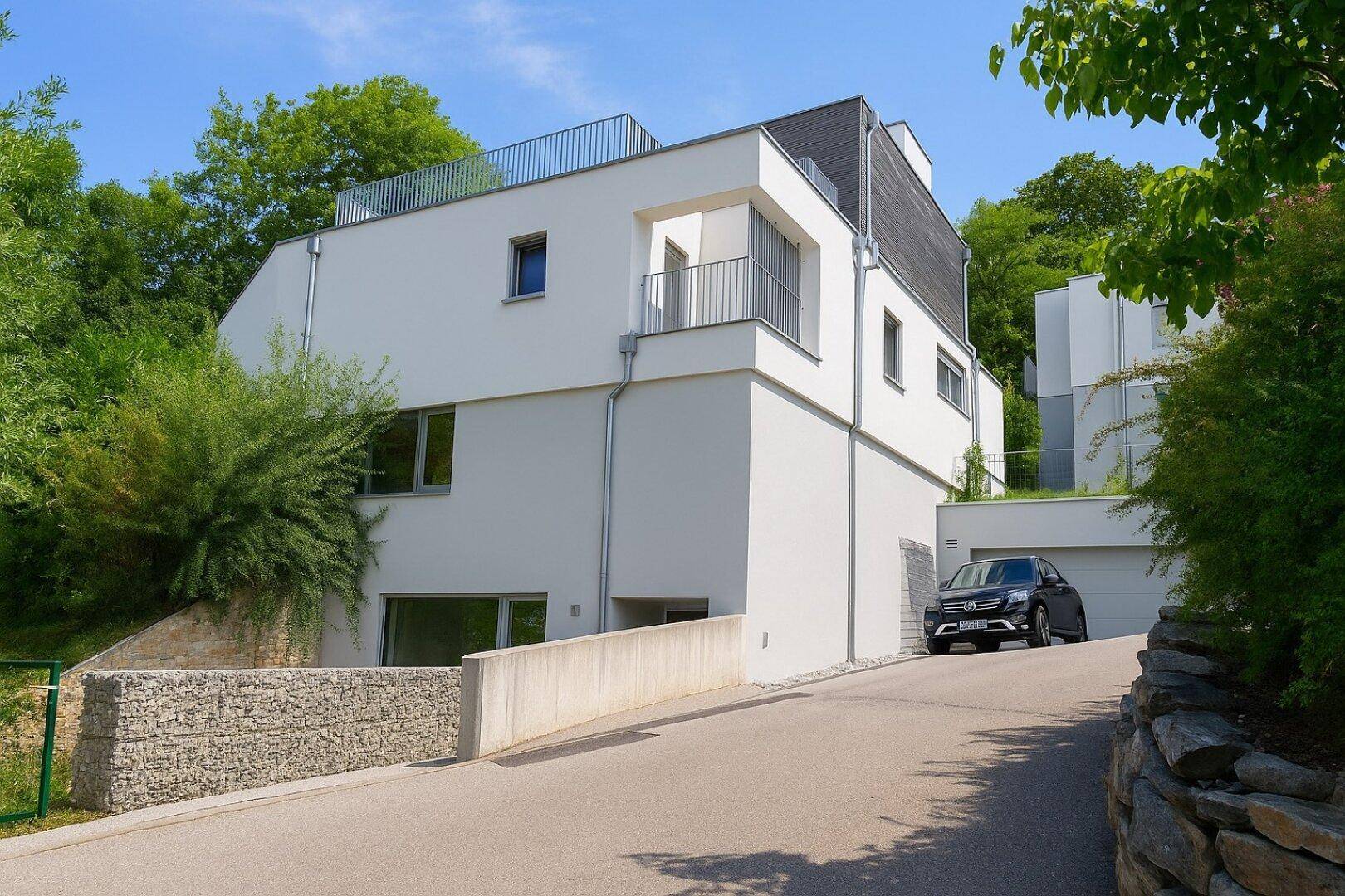 Moderne Villa mit weißer Fassade, Flachdach und integrierter Garage in grüner Umgebung.