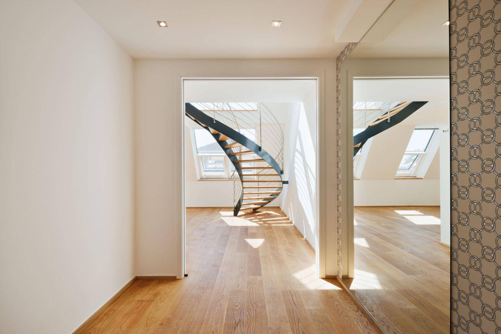 Lichtdurchfluteter Flur mit Holzparkett und Blick auf eine moderne Wendeltreppe.