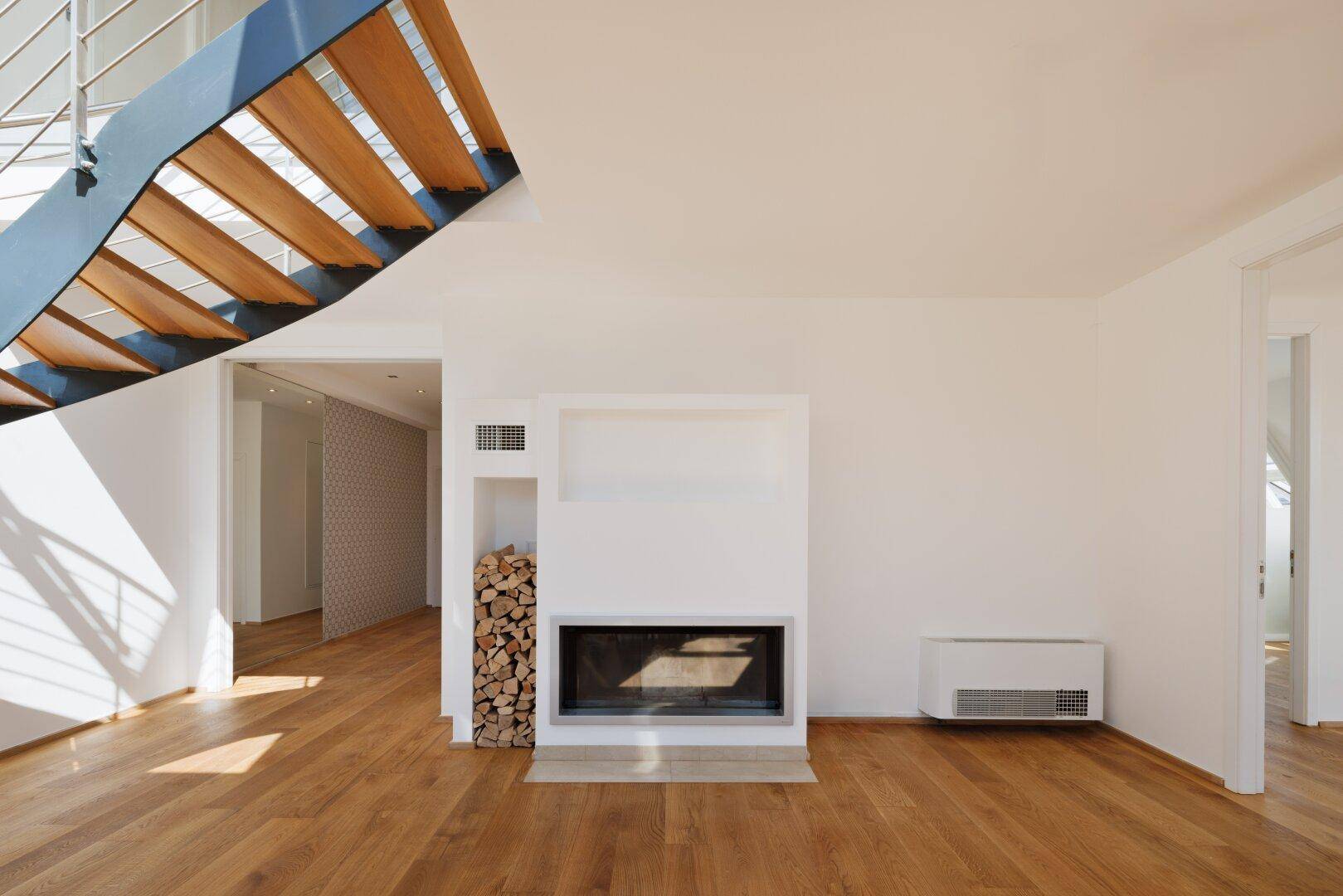 Heller Wohnbereich mit modernem Kamin, Holzparkettboden und eleganter Treppe.