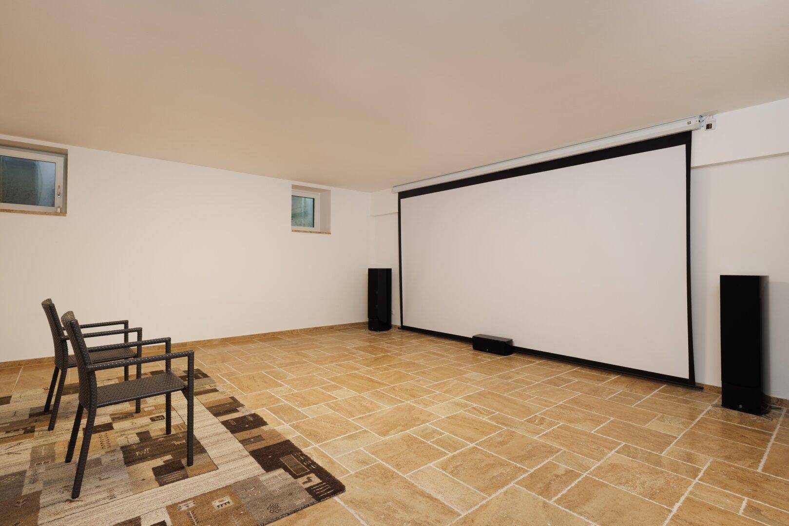 Geräumiger Medienraum im Untergeschoss mit großer Leinwand und Fliesenboden, ideal für Filmabende.